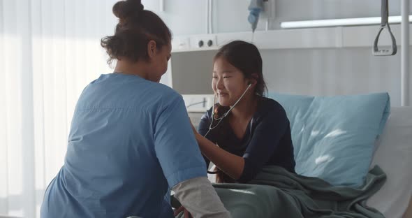 Teenage Asian Kid Patient Using Stethoscope Listening to Nurse Heartbeat in Hospital Ward