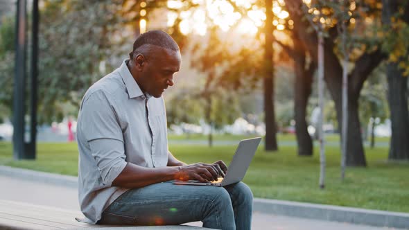 Elderly African American Man Sitting Outdoors Browsing Wireless Internet on Modern Device Typing