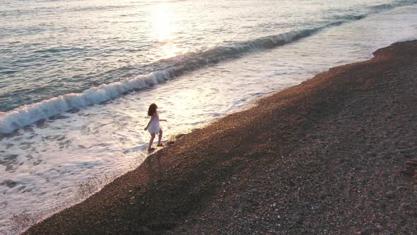 Drone View Panning Shot of Excited Woman Running Spinning on Mediterranean Sea Coast at Sunset