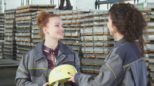 Beautiful Female Factory Worker Receiving a Hardhat from Her Colleague