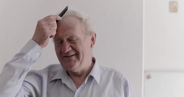 Cheerful Senior Man Combs His Gray Hair and Laughs at Camera on the Background
