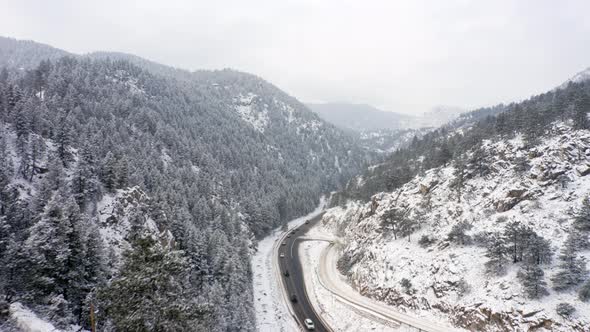 Aerial reveal backwards of Boulder Canyon Drive in Colorado during the winter as cars drive down icy