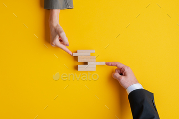 s of businessman and businesswoman pushing wooden peg in a stack of them. Over yellow background, with copy space.