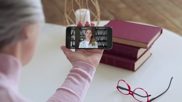 Over the Shoulder View of an Elderly Woman Video Call of a Young Daughter Using a Smartphone. The