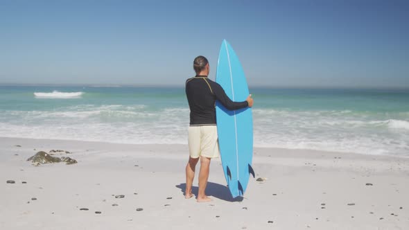 Senior Caucasian man holding a surfboard on the beach