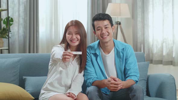 Happy Asian Couple Smiling To Camera After Find Out Positive Pregnancy Test In Living Room At Home