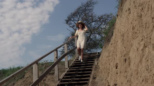 Energetic Woman Hurrying Downstairs Sand Beach Holding Straw Hat on Head