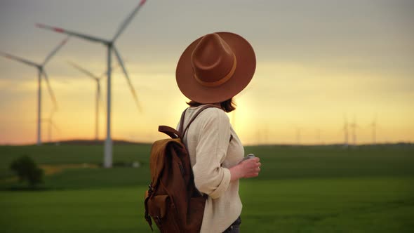 Young woman with a retro camera looking at a wind farm in a field