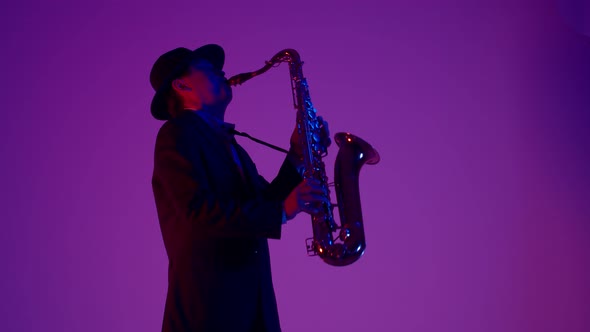 Male musician in black suit and hat plays a gold saxophone the studio with changing color gradient