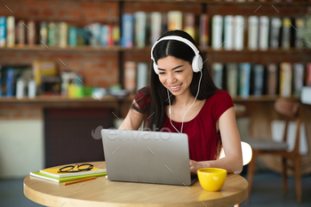 With Laptop And Headphones In Cafe, Watching Webinar Or Online Tutorials, Looking At Computer Screen And Smiling, Enjoying Distance Learning