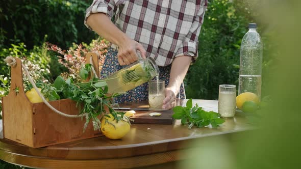 Woman Pours Summer Refreshing Lemonade Into Glass Outdoors