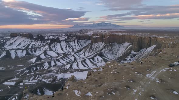 Flying backwards past people on the edge of a cliff at sunrise