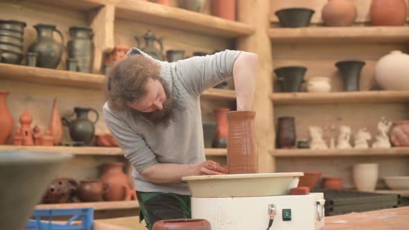 Potter forms an earthenware jug in his workshop. A bearded man works with clay