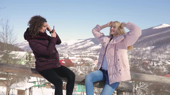 Two Girls Friends Photographing Each Other on Snowy Mountains Background