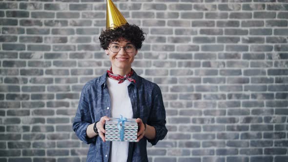 Portrait of Cheerful Young Woman in Bright Party Hat Holding Gift Box Smiling