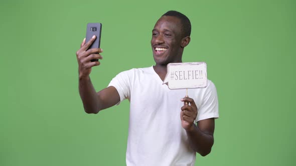 Young African Man Taking Selfie with Paper Sign Against Green Background