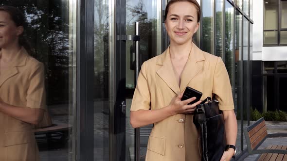 Caucasian Confident Young Business Woman is Talking on Phone Outside near Modern Office Building