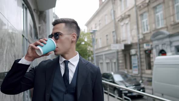 Man in Suit with Sunglasses Drinks a Cup of Beverage When Looks Around on Street