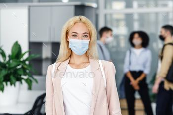 d protects against virus. Focus on attractive blonde woman in protective mask and business suit, employees on blurred office background
