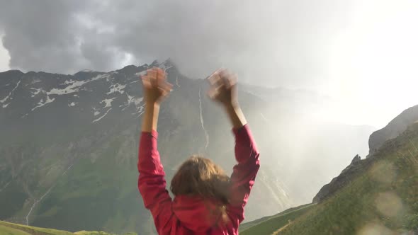 Happy Female Traveler Jumps for Joy with Her Hands Up in the Rain in the Mountains During Sunset