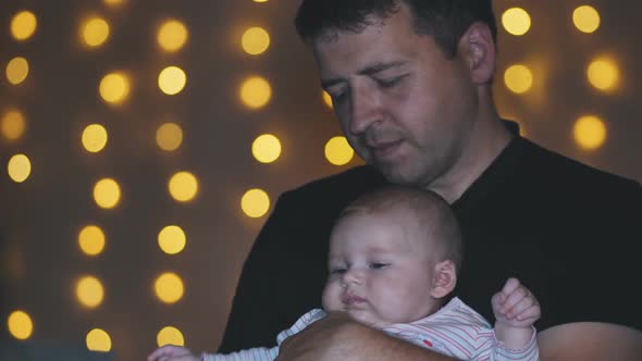 A Father Kisses His Child in His Arms at the Evening Lights