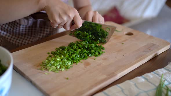 Woman chopping green onion on wooden board in kitchen