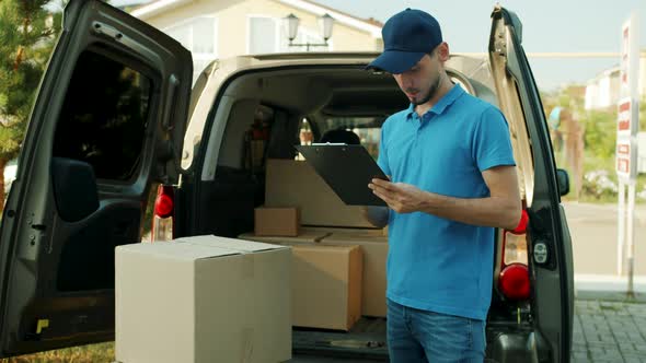 Commercial Deliveryman Working with Papers Looking at Boxes in Van Delivering Eshop Orders