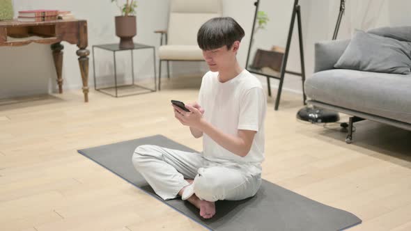 Young Asian Man Using Smartphone on Yoga Mat at Home