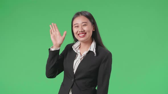 A Smiling Asian Business Woman Waving Hand Saying Good Bye While Walking Through Green Screen