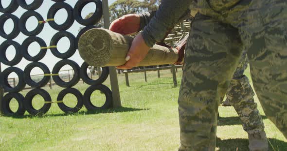 Diverse fit group of soldiers lifting and carrying tree log in the sun at army obstacle course