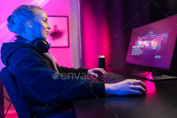 gamer woman with headset and tattoos streaming live while playing multiplayer online video game on her PC. Blue and pink colored LED lights.