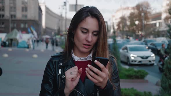 Shocked Woman Holding Smartphone of the Blurred City Background 