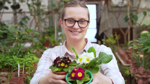 Young Woman Sniffs Pots of Flowers and Holds Them Out