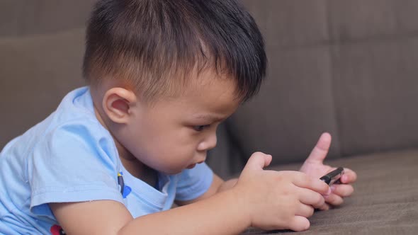 Little Boy Laying On A Sofa Plays With Smartphone