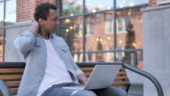 African Man with Neck Pain Using Laptop Outdoor