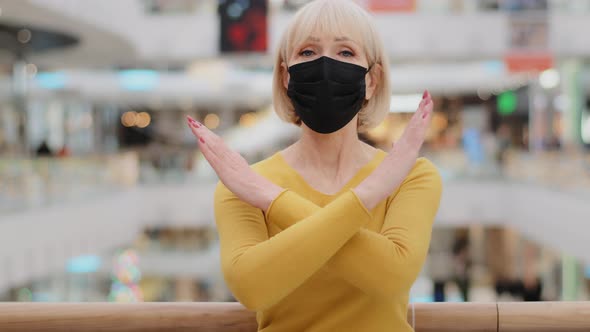 Serious Upset Mature Woman in Medical Mask Stands in Public Place Looking at Camera Arms Crossed in