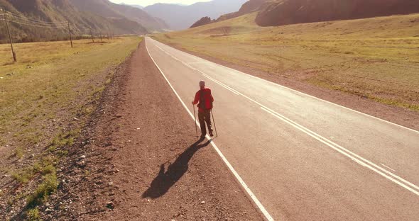 Flight Over Hitchhiker Tourist Walking on Asphalt Road. Huge Rural Valley at Summer Day. Backpack