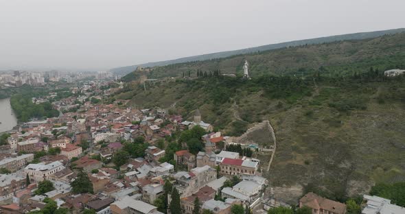 Slow aerial shot of the Old Tbilisi neighborhood and Kartlis Deda in the back.