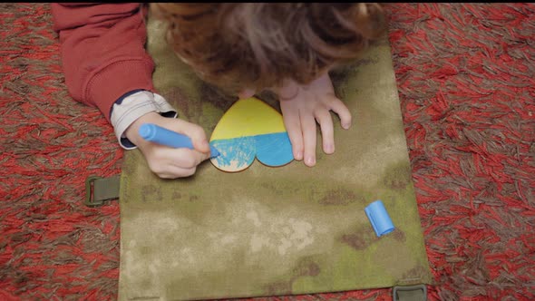 A child paints a heart in the colors of the flag of Ukraine, top view