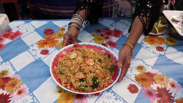 Old Hands Serve Plate of Shrimp Stir Fry on Floral Table Cloth - Dolly and Jib In