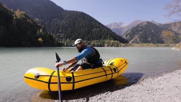 Man is Paddling on Raft Boat in the Mountain Lake