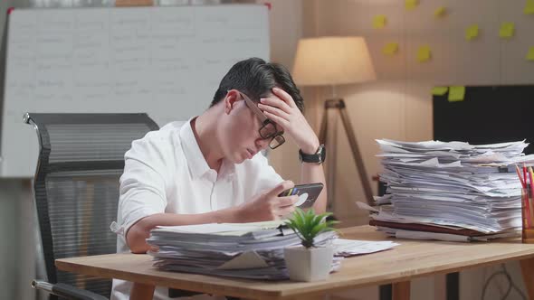 Asian Man Being Upset Losing Game On Smartphone After Working With Documents At The Office