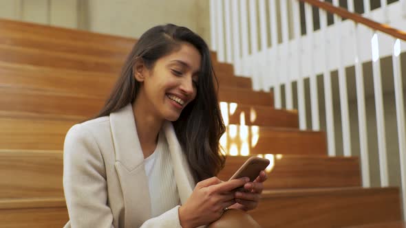 Slow motion shot of smiling woman using smartphone on stairs