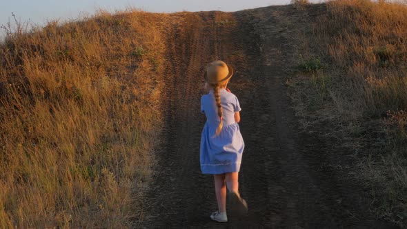 Adorable little girl in blue summer dress climbing up the hill. Child running countryside