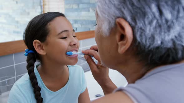 Grandmother helping granddaughter to brush her teeth in the bathroom