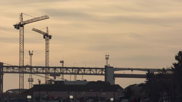 Construction cranes next to the 25Th Lisbon Bridge in the sunset. Suspension Bridge connecting the c