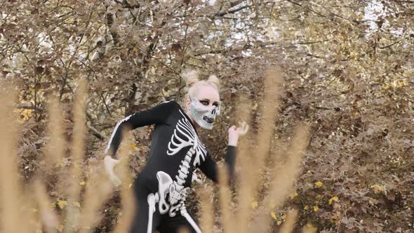 A girl with a scary make-up in a skeleton costume, in a mask with rhinestones in a gloomy autumn for
