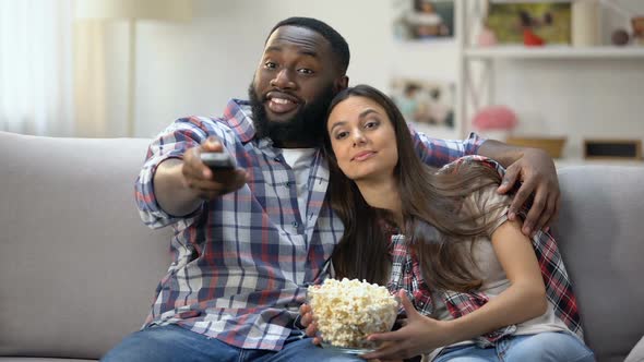 Multiethnic Couple With Pop Corn Switching Channels, Watching TV Program at Home