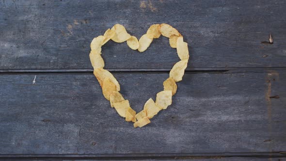 Potato chips forming a heart shape with copy space on wooden surface