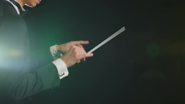 Symphony Orchestra Conductor Wearing Suit is Directing Musicians with Movement of Baton on Black